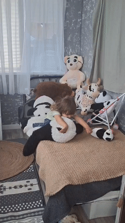Toddler plays with stuffed pandas on bed in Russia