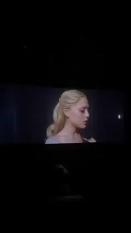 The video shows a movie theater screen displaying a scene from a fantasy film. The scene depicts a mountainous landscape with flying creatures resembling large birds with blue and white feathers. The creatures are soaring through a canyon or valley with rock formations and mist. The theater is dark, and the person filming is sitting in a seat, with the back of the seat visible in the foreground.