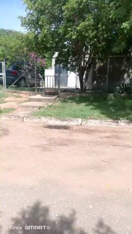 The video shows a street scene during daylight. Initially, a fence and part of a house are visible behind it. The camera then pans to the right, revealing more of the street and houses along it. A white pickup truck is parked on the side of the road, with its driver's side door open. The sky is blue with some clouds.