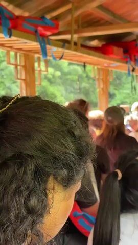The video shows a group of people on a covered boat. They are standing and it appears they are about to depart or have just departed. Overhead, orange life jackets hang from the wooden rafters. A sign is visible saying "Please wear (take) a life jacket" in both Chinese and English. Through the sides of the boat, green trees and a small building on the water are visible.