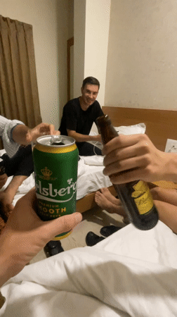 Three men toast drinks in Kolhapur hotel room