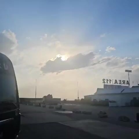 The video shows a cloudy sky with the sun peeking through a gap in the clouds. There is a building with a sign that reads "ARENA". There is also a truck and some concrete barriers. The scene appears to be an outdoor area, possibly a parking lot or a loading dock.