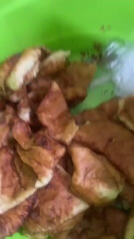 A pile of fried dough pastries is shown in a green bowl. The pastries are golden brown and appear to be slightly puffy. Some are folded or crinkled, while others are flatter. A plastic bag is visible in the upper right corner of the bowl, containing white material. The background is a bright green bowl.