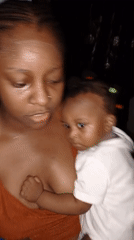 Mother holds baby while using phone in Keffi