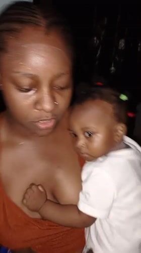 Mother holds baby while using phone in Keffi