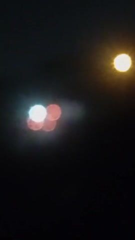 The video depicts blurry lights in the dark. Initially, there are five blurry circles: one white, three red, and one yellow. As the video progresses, the shapes and arrangement of the lights shift slightly. By the end of the clip, only two red blurry circles remain visible, along with the faint outline of white.
