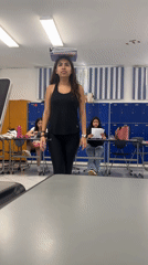 Woman balances notebooks on head, makes funny face in classroom