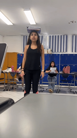 Woman balances notebooks on head, makes funny face in classroom