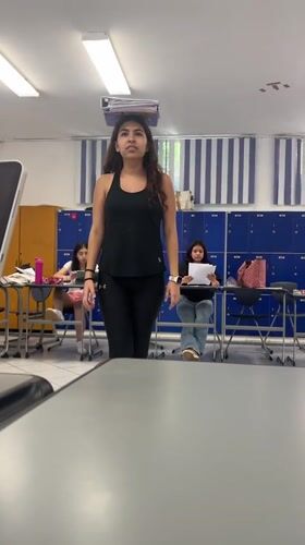 Woman balances notebooks on head, makes funny face in classroom