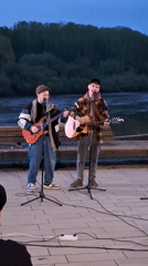 Two musicians perform riverside concert at dusk in Glazov