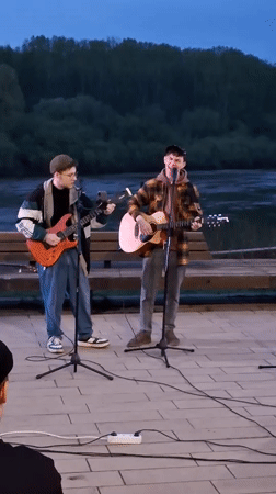 Two musicians perform riverside concert at dusk in Glazov