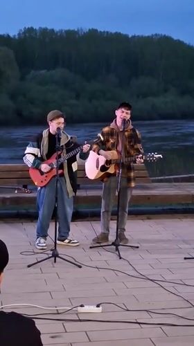 Two musicians perform riverside concert at dusk in Glazov