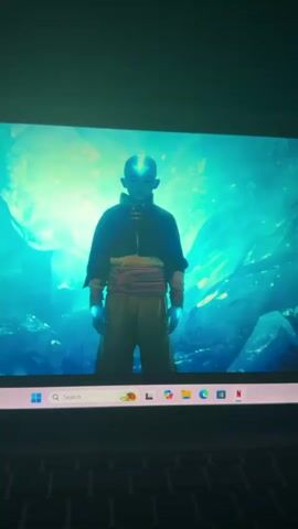 The video shows a scene from the TV show "Avatar: The Last Airbender" playing on a laptop. The first shot features Aang in the Avatar state, surrounded by blue energy. The next shot shows Katara and Sokka in arctic clothing sitting in the snow. The laptop is open and the Windows taskbar is visible at the bottom of the screen. Subtitles reading "[mystical whirring]" appear on the screen.