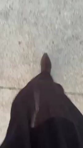 The video shows a first-person perspective of someone walking on a concrete surface. The person is wearing a long, black, semi-transparent garment and brown boots. The camera view is mostly focused on the garment and the ground as the person walks. A white object and a red-tipped object are briefly visible on the ground in the lower right corner of the frame.