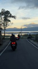 Three motorbikes travel waterside road in Kintamani, Indonesia
