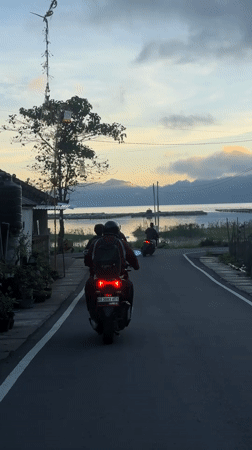 Three motorbikes travel waterside road in Kintamani, Indonesia