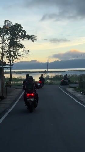 Three motorbikes travel waterside road in Kintamani, Indonesia