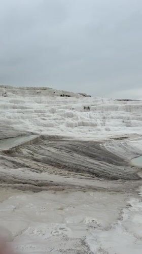 Tourists explore Pamukkale's white travertine terraces on overcast morning