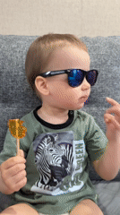 Toddler with sunglasses enjoys lollipop on couch in Rusanovo