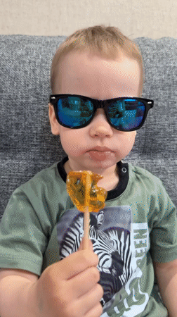Toddler with sunglasses enjoys lollipop on couch in Rusanovo