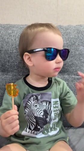 Toddler with sunglasses enjoys lollipop on couch in Rusanovo