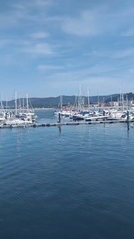 A video pans across a harbor filled with sailboats and a town on a hill in the background. The camera then focuses on the interior of a boat, showing rows of empty seats and a metal railing along the side. The video ends as the camera moves further into the boat's interior.