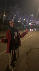 Person in red jacket explores nighttime marina with Russian vessels
