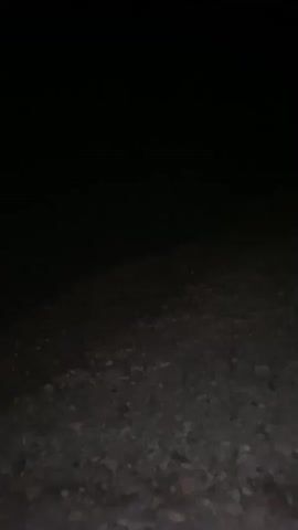 The video shows a dark, gravelly surface with a black background. The camera is moving, creating a slight blur. There are no people or visible objects other than the gravel and the dark background. The lighting is very low, suggesting it is nighttime or a very dark environment.