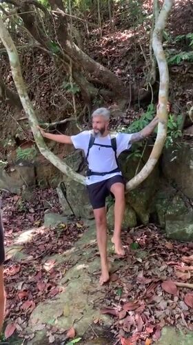 Hiker rests on tree branch near waterfall in Thailand
