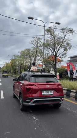 Person stands through sunroof of moving car in Denpasar