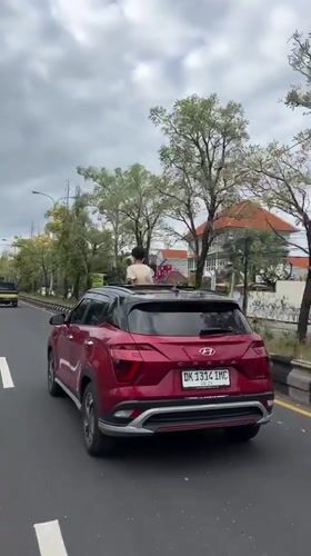 Person stands through sunroof of moving car in Denpasar