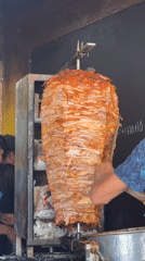 Street vendor prepares rotisserie meat near vintage car in Puebla