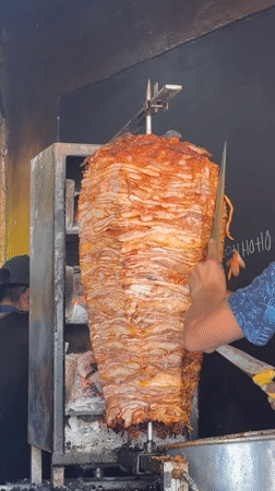 Street vendor prepares rotisserie meat near vintage car in Puebla
