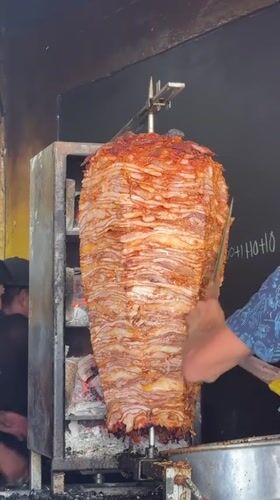 Street vendor prepares rotisserie meat near vintage car in Puebla