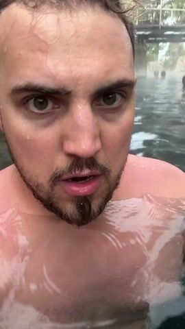 The video shows a man in a pool. He is looking at the camera and talking, then goes underwater, showing the bottom of the pool. The bottom of the pool is rocky and green. A ladder is also visible at the bottom.