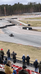 Car navigates racetrack turn in overcast Rīga morning