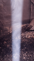 Water stream observed falling onto dirt ground in enclosed space
