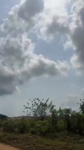 The camera pans upwards from a low-lying dirt track and some greenery, towards a sky filled with puffy white and gray clouds. At one point a solar-powered street light is visible against the cloudy sky.