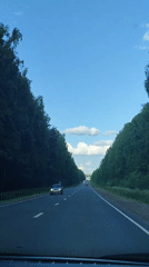 Midday highway traffic recorded amid green trees, blue skies