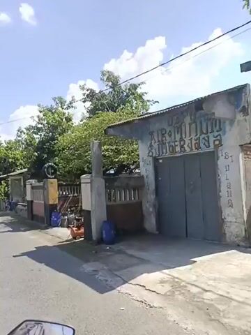 A first-person video shows a journey down a quiet residential street, lined with houses and green trees, under a bright blue sky with scattered clouds. The camera moves at a steady pace, showcasing the peaceful neighborhood on a sunny day.