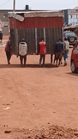 Men Transport Large Structure Through Nigerian Village Streets