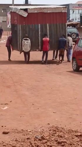 Men Transport Large Structure Through Nigerian Village Streets
