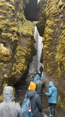 Tourists visit Seljalandsfoss waterfall in Iceland wearing rain gear