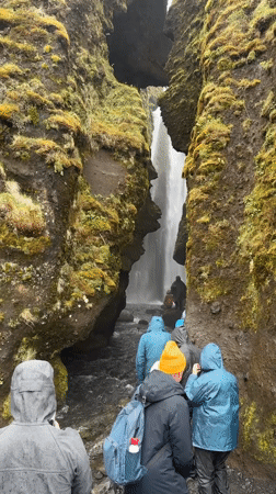 Tourists visit Seljalandsfoss waterfall in Iceland wearing rain gear