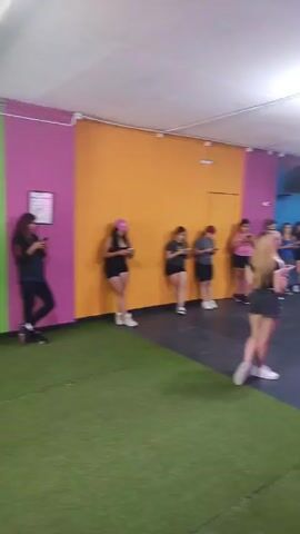 The video shows a large room with a group of people standing around, looking at their phones. The room has brightly colored walls, with a large "Interval" sign on one wall. There are a few men who appear to be instructors, and they are interacting with each other. The environment appears to be a fitness studio or gym.