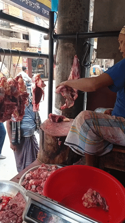 Butcher cuts meat at outdoor Dhaka market stall