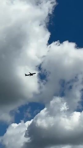 An airplane is flying high in the sky on a sunny day with white puffy clouds.