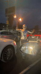 Silver-painted fire performer approaches cars in Cholula street