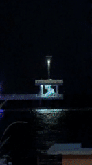 Nighttime waterfront gathering documented at illuminated pavilion and pier