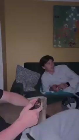 Here is a concise description of the video:

The video shows a living room with yellow walls. A man is lying on a green sofa with a navy blue bag next to him. There's a painting on the wall above the sofa. Another painting hangs above an electric fireplace on the opposite wall, where a TV is also visible. The room is dimly lit.
